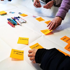 Mesa conrotuladores y hojas de posits sueltas con ideas escritas, y manos seleccionando